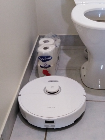 A robot vacuum cleaner in a toilet with a pack of toilet paper rolls blocking its path